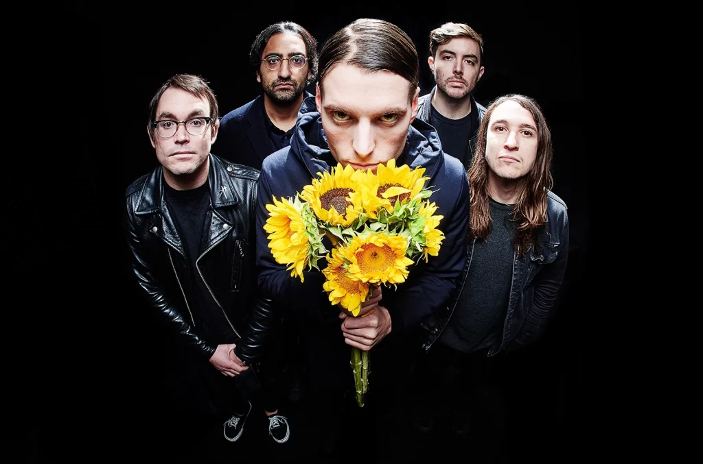 Imagem da banda Deafheaven com fundo preto e vocalista segurando girassóis.