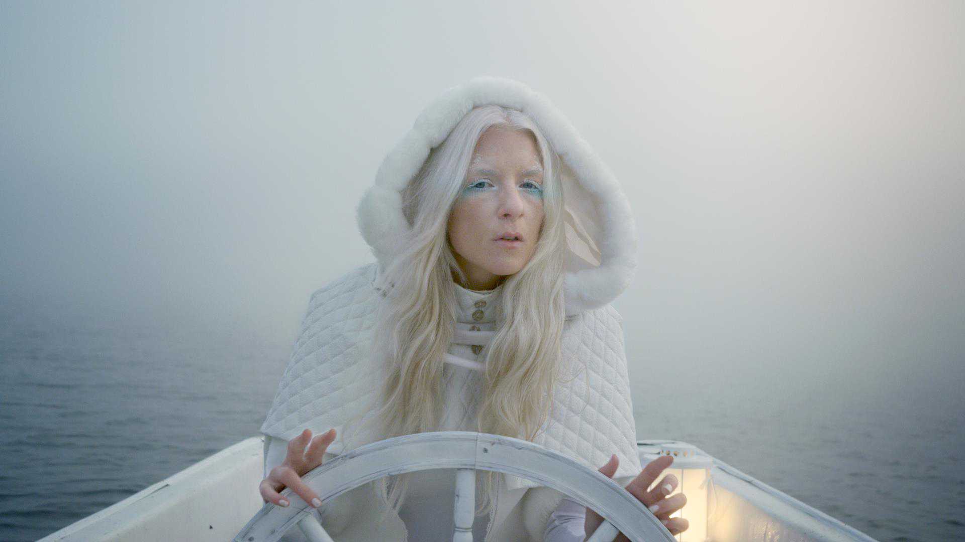 Imagem da cantora iamamiwhoami em um barco vestindo roupas brancas de frio